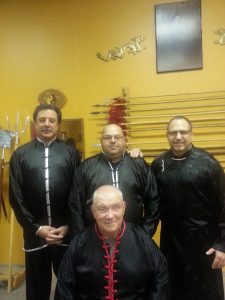 Senior instructor with three students standing before the weapons wall