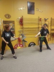 Two students sparring with training weapons, facing off