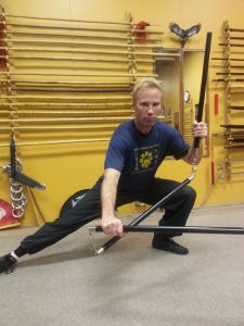 Student in a low lunge stance holding two weapons crossed