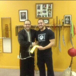 Instructor presenting a certificate to a student in front of the weapons wall