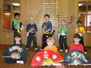 Seven children in uniform holding fans and weapons for a youth class photo