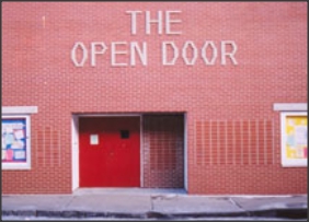 Brick storefront with a sign reading The Open Door above red double doors